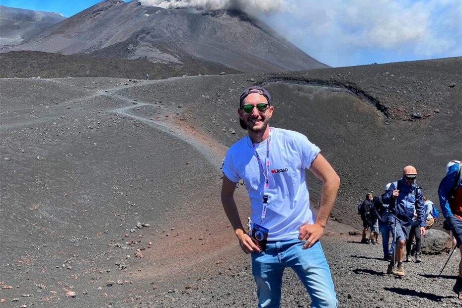 Turista sorridente davanti a un vulcano attivo.