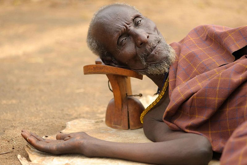 Anziano riposa a terra appoggiato a sgabello.
