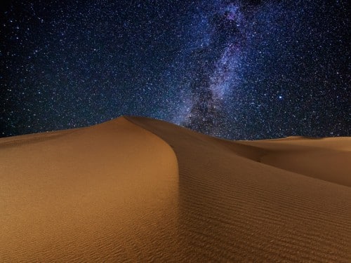 Deserto sabbioso sotto un cielo stellato notturno.