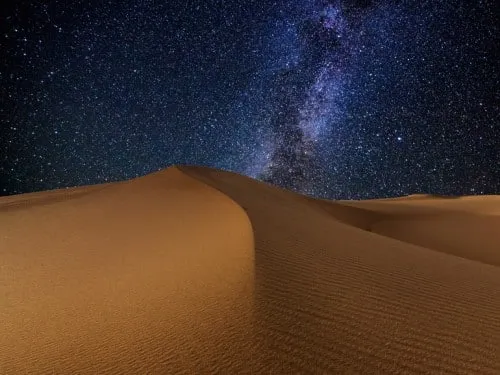 Deserto sabbioso sotto un cielo stellato notturno.