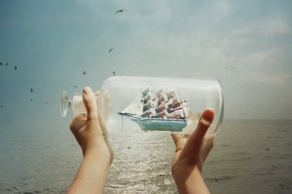 Mani tengono nave in una bottiglia, mare sfondo.
