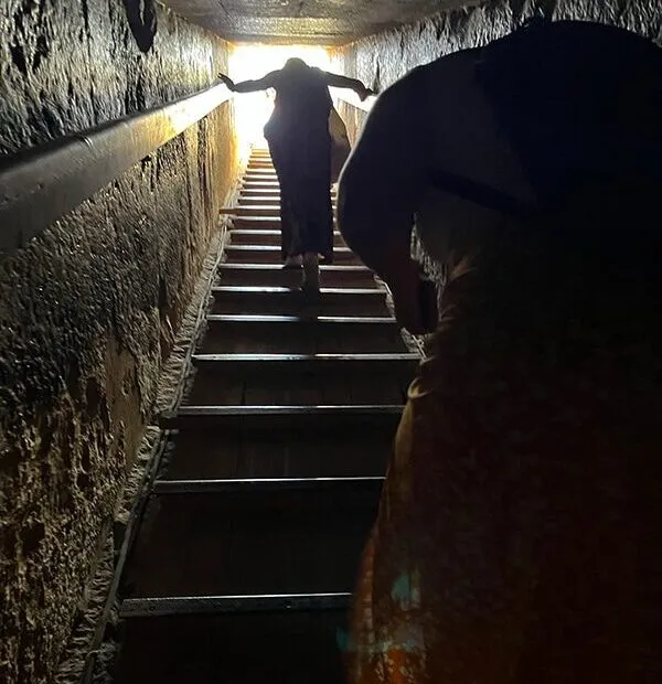 Persone salgono stretta scala verso luce.