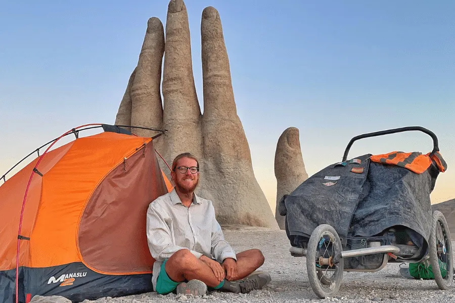 Escursionista sorride accanto a tenda in paesaggio desertico.