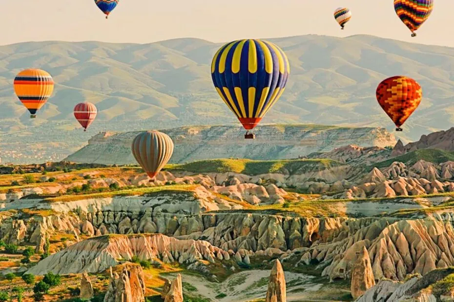 Mongolfiere colorate sorvolano paesaggio collinare roccioso.