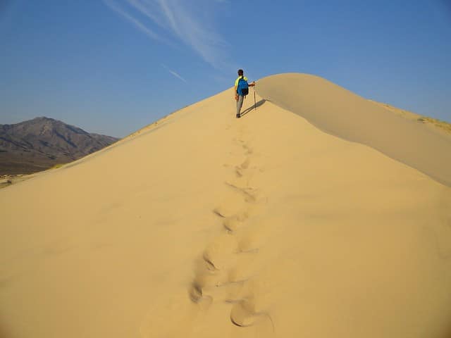 Escursionista su duna nel deserto con impronte.