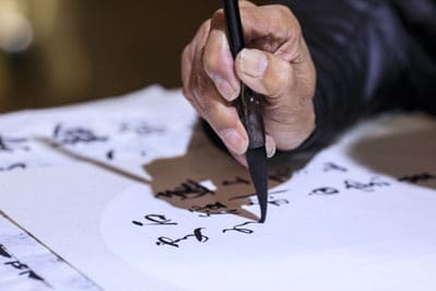 Persona che pratica calligrafia orientale con pennello.