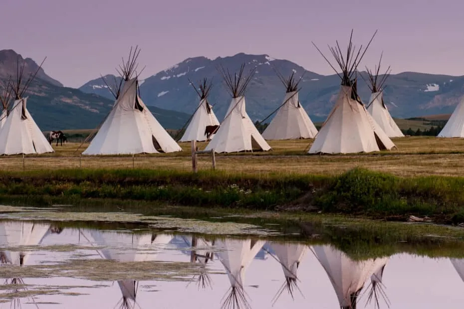Teepee riflessi su acqua al tramonto.